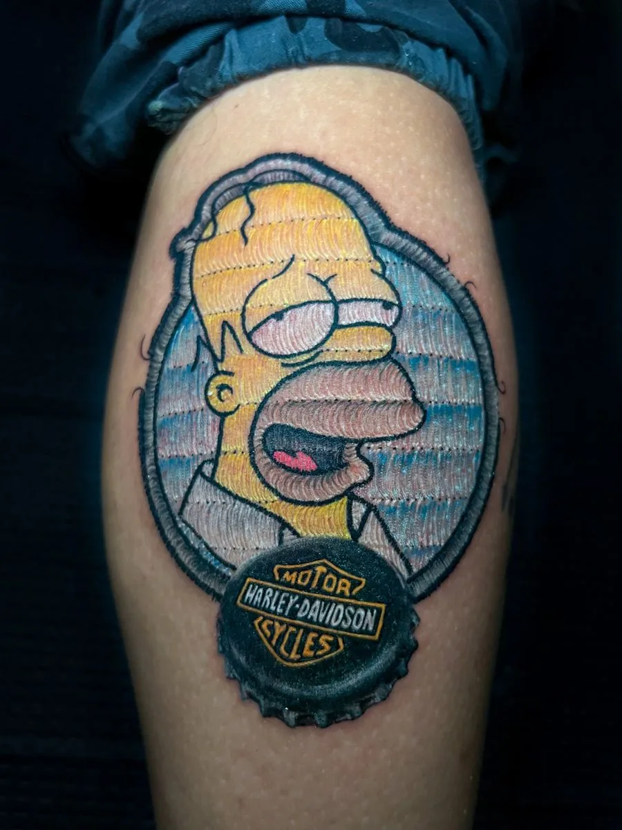 Tatuaje estilo parche bordado: personaje de caricatura con borde bordado y una chapa de botella, en la pierna