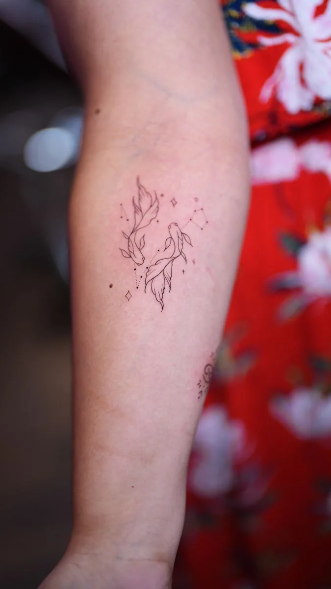 Fine line tattoo: two fish with stars, on the forearm