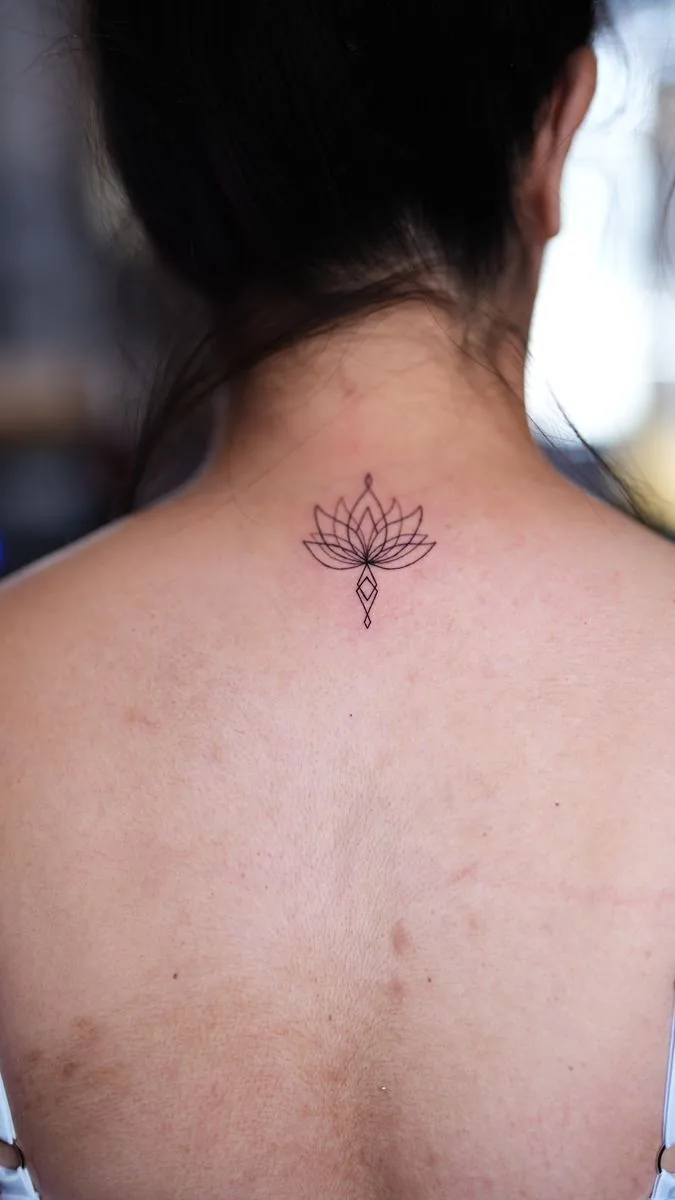 Fine line tattoo: lotus flower on the upper back, below the neck